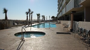 Un área de piscina con sillones reclinables y una piscina pequeña, rodeada de palmeras y un edificio con balcones.