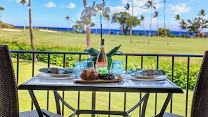 Une table dressée avec des assiettes, une bouteille et une orchidée décorative, sur un balcon offrant une vue sur un terrain de golf et des palmiers.