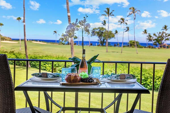 A table set with plates, a bottle, and a decorative orchid on a balcony with a view of a golf course and palm trees.