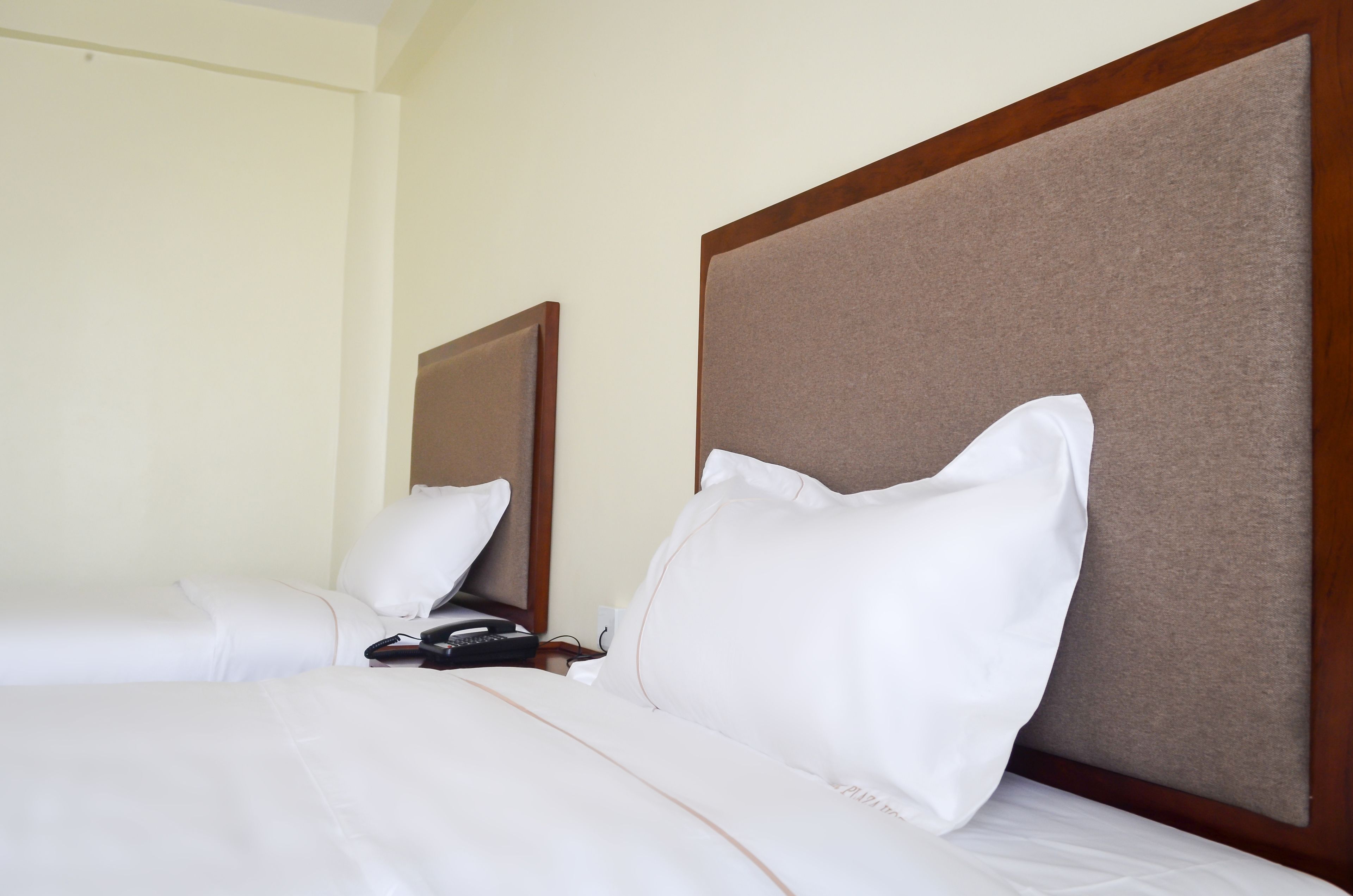 A hotel room with two beds, each with white bedding and a wooden headboard.