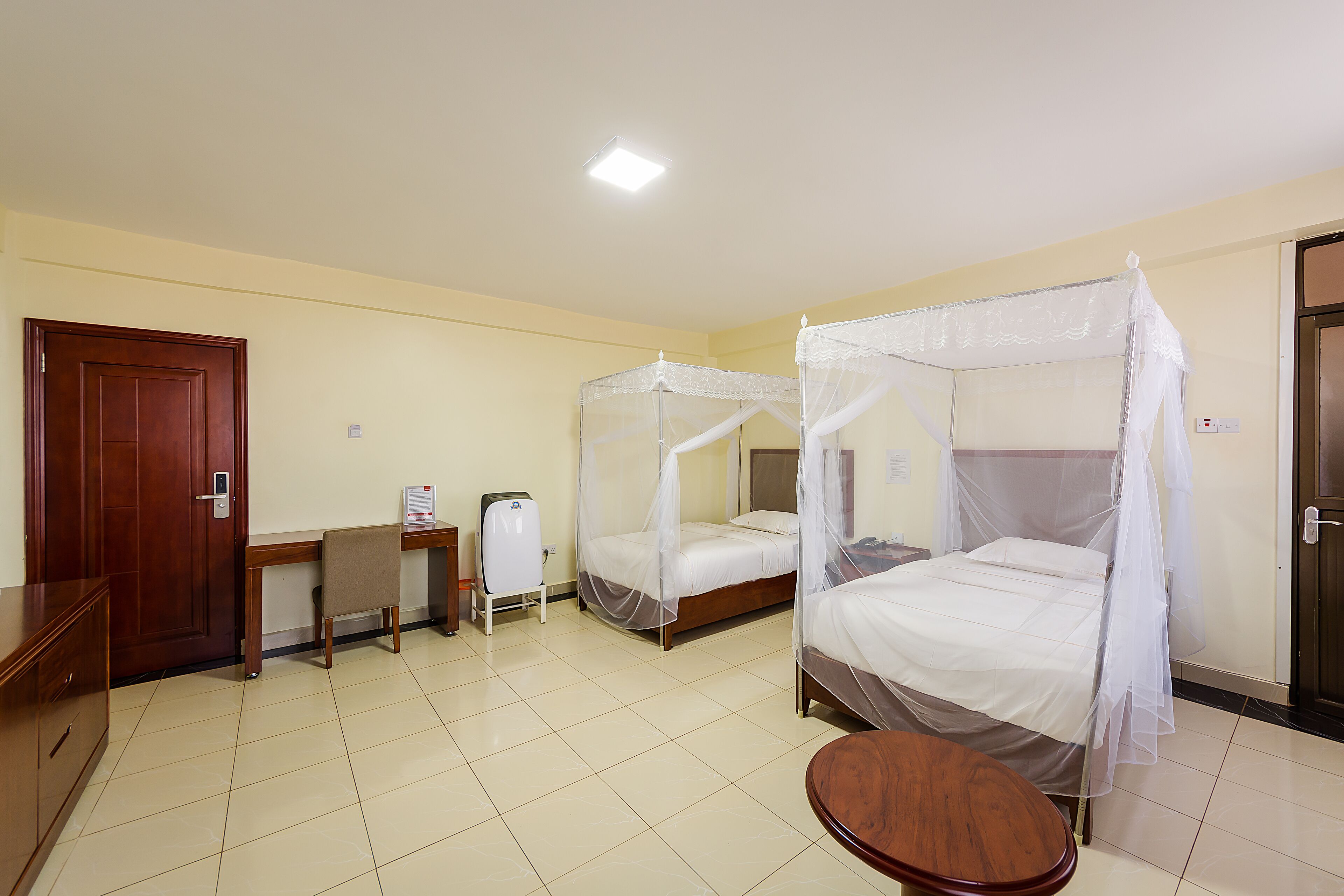 A hotel room with two beds, a desk, a chair, and a small table.