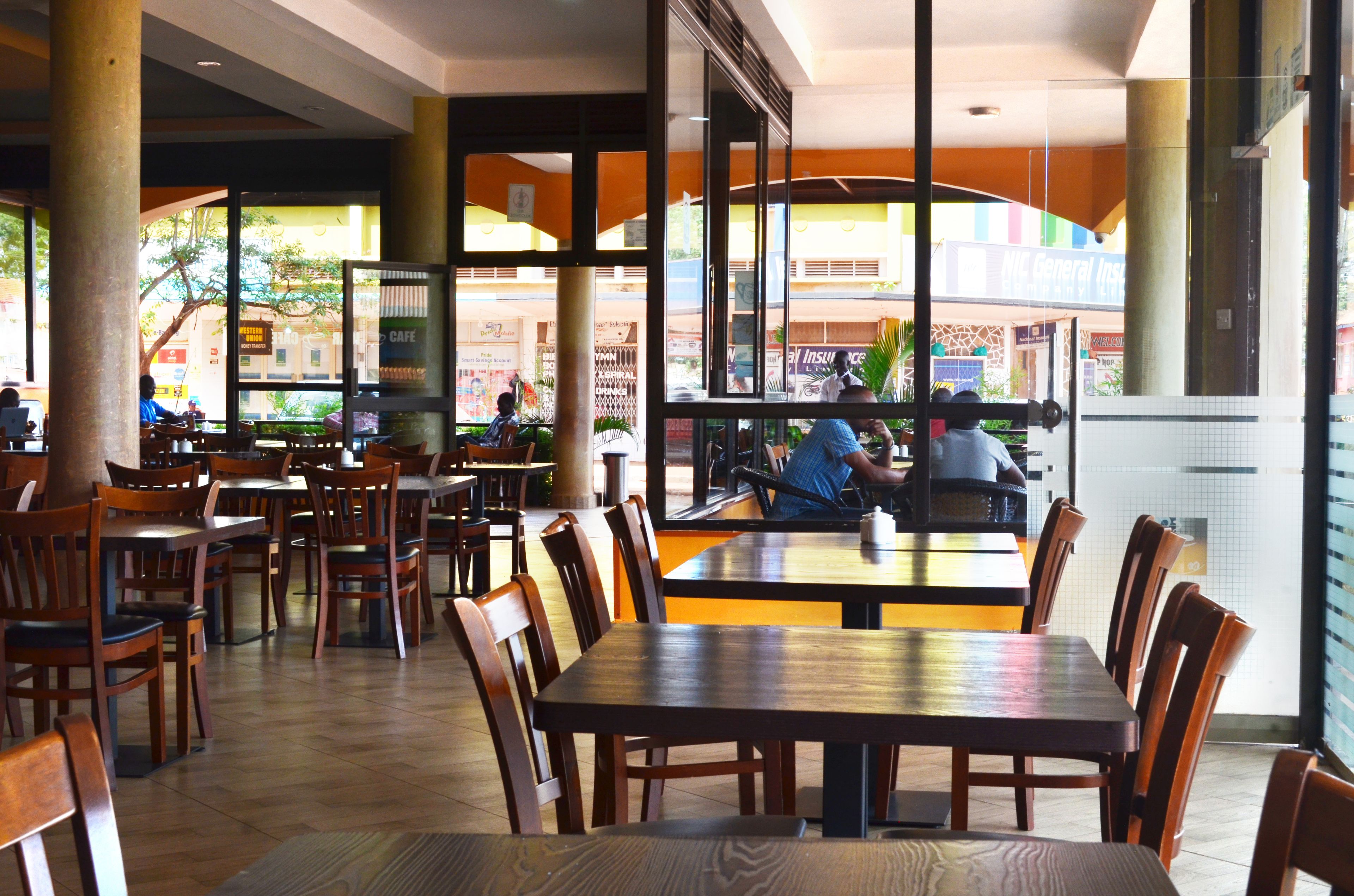 Un vaste espace de restauration intérieur, doté de nombreuses tables et chaises en bois, de grandes fenêtres donnant sur la rue et d’un comptoir central.