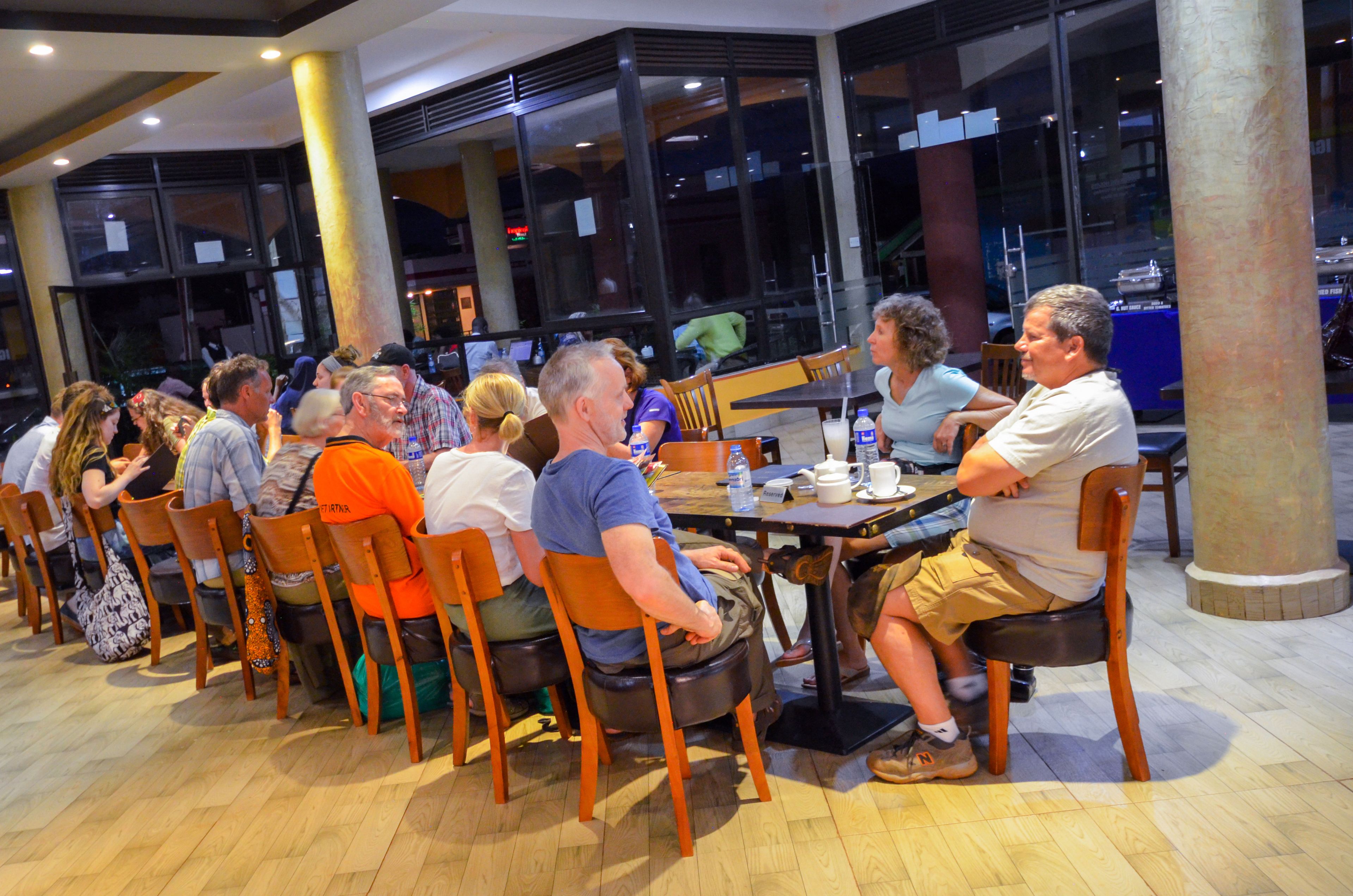A group of people seated at tables in a spacious indoor area with large windows and wooden chairs.
