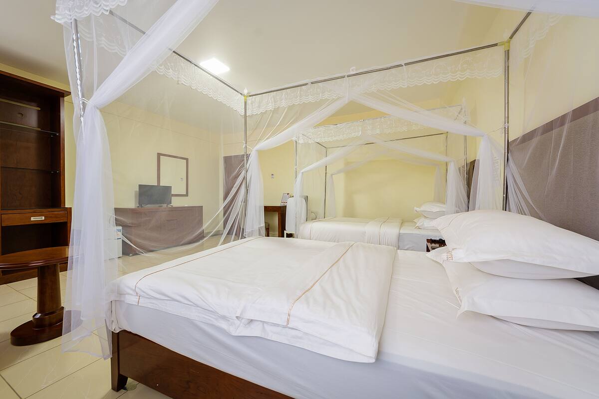 A neatly made bed with white linens and a canopy, a wooden nightstand, and a mirror on the wall.