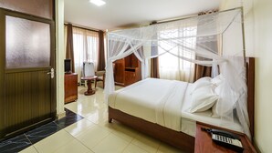A hotel room with a bed, a bedside table with a telephone, a wooden wardrobe, a desk with a chair, and a door with frosted glass panels.