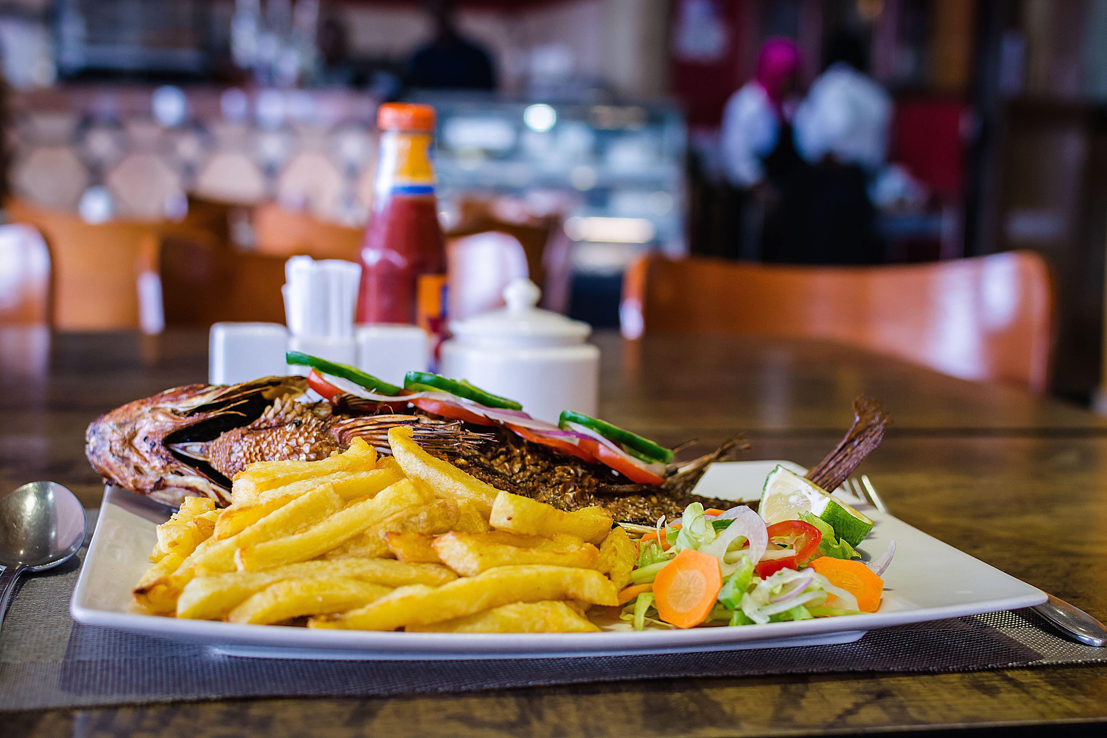 A plate of food including a whole fish, French fries, and a salad.