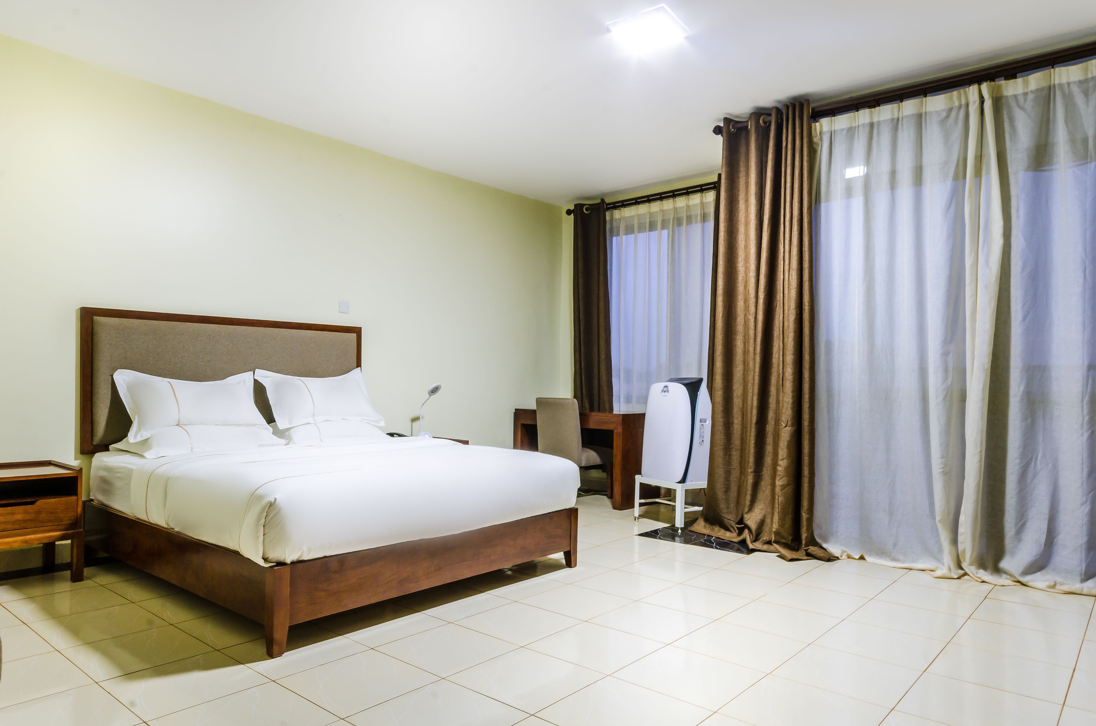 Ein Hotelzimmer mit einem großen Bett, einem Schreibtisch, einem Stuhl und einem Fenster mit Vorhängen.