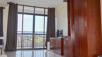 A room with a large sliding glass door leading to a balcony, a wooden wardrobe, and a small table with a television.