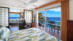 A hotel room with a bed, a desk, a chair, and a balcony with a view of the ocean.