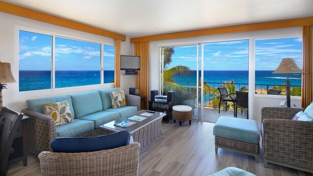 A spacious living area with a large window overlooking the ocean, wicker furniture, and a flat-screen TV.
