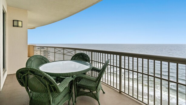 A balcony with a round table and wicker chairs, overlooking the ocean.