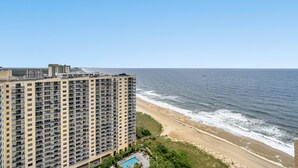 A high-rise hotel with a beach view, featuring multiple balconies and a pool area.