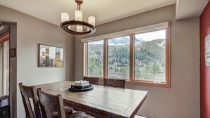 A dining area with a large wooden table, chairs, and a view of a forest through large windows. - Spacious Centrally Located/Short Walk to the Lifts/Hot Tub Access (Keystone)