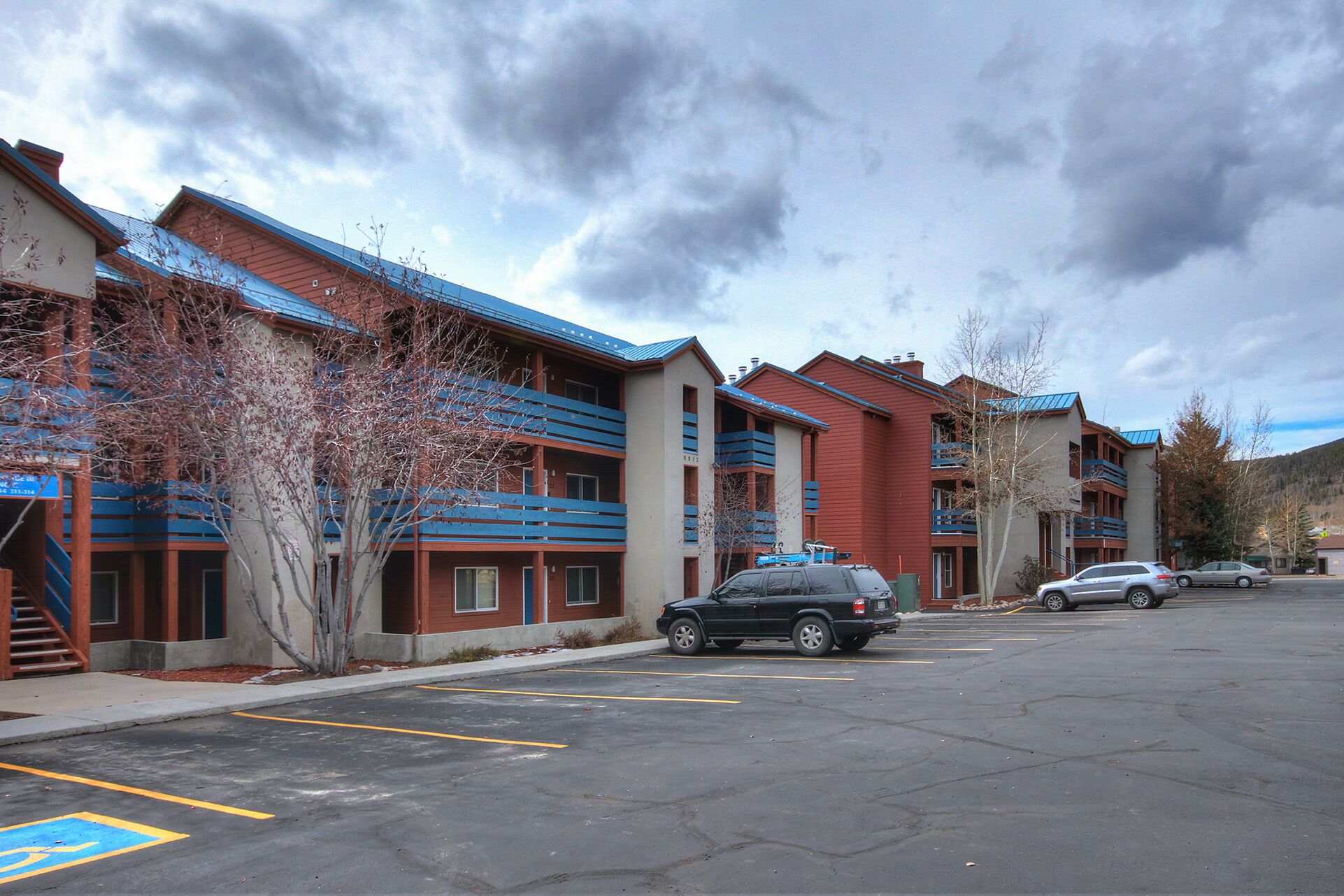 A parking lot with several cars, a building with red and blue exterior, and a clear sky.