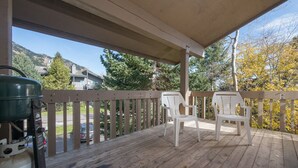 A covered deck with wooden railings, two white plastic chairs, and a propane tank. - JHRL - Nez Perce B6 - Great location near pool and hot tub access (Teton Village)