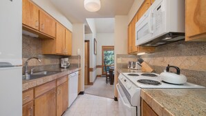 A compact kitchen with wooden cabinets, a built-in stove, and granite countertops. - JHRL - Nez Perce B6 - Great location near pool and hot tub access (Teton Village)