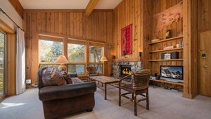A cozy log cabin interior with a fireplace, leather sofa, and a television. - JHRL - Nez Perce B6 - Great location near pool and hot tub access (Teton Village)