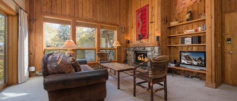 A cozy log cabin interior with a fireplace, leather sofa, and a television.