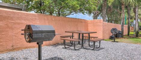 An outdoor patio with a grill, picnic table, and benches.