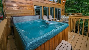 Une terrasse en bois avec un jacuzzi, des sièges d’extérieur et une vue sur les arbres environnants.