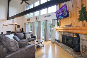 A spacious living room with a fireplace, a large flat-screen TV mounted on the wall, and a cozy seating area with a leather couch. - Dogs welcome, hot tub, pool table, Gatlinburg! (Gatlinburg)