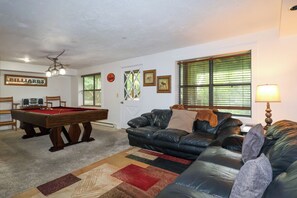 A living room with a pool table, a leather couch, and a window with blinds.