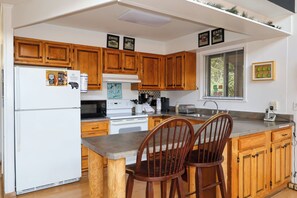 A kitchen with wooden cabinets, a refrigerator, a stove, a microwave, a sink, and two bar stools.