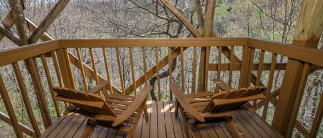 A wooden deck with two Adirondack chairs facing a forested area.