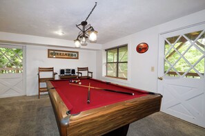 A pool table with balls, a wooden chair, a television, and a framed sign on the wall.