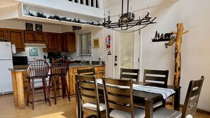 Un coin repas avec une table et des chaises en bois, une cuisine en arrière-plan et un poteau décoratif en bois.