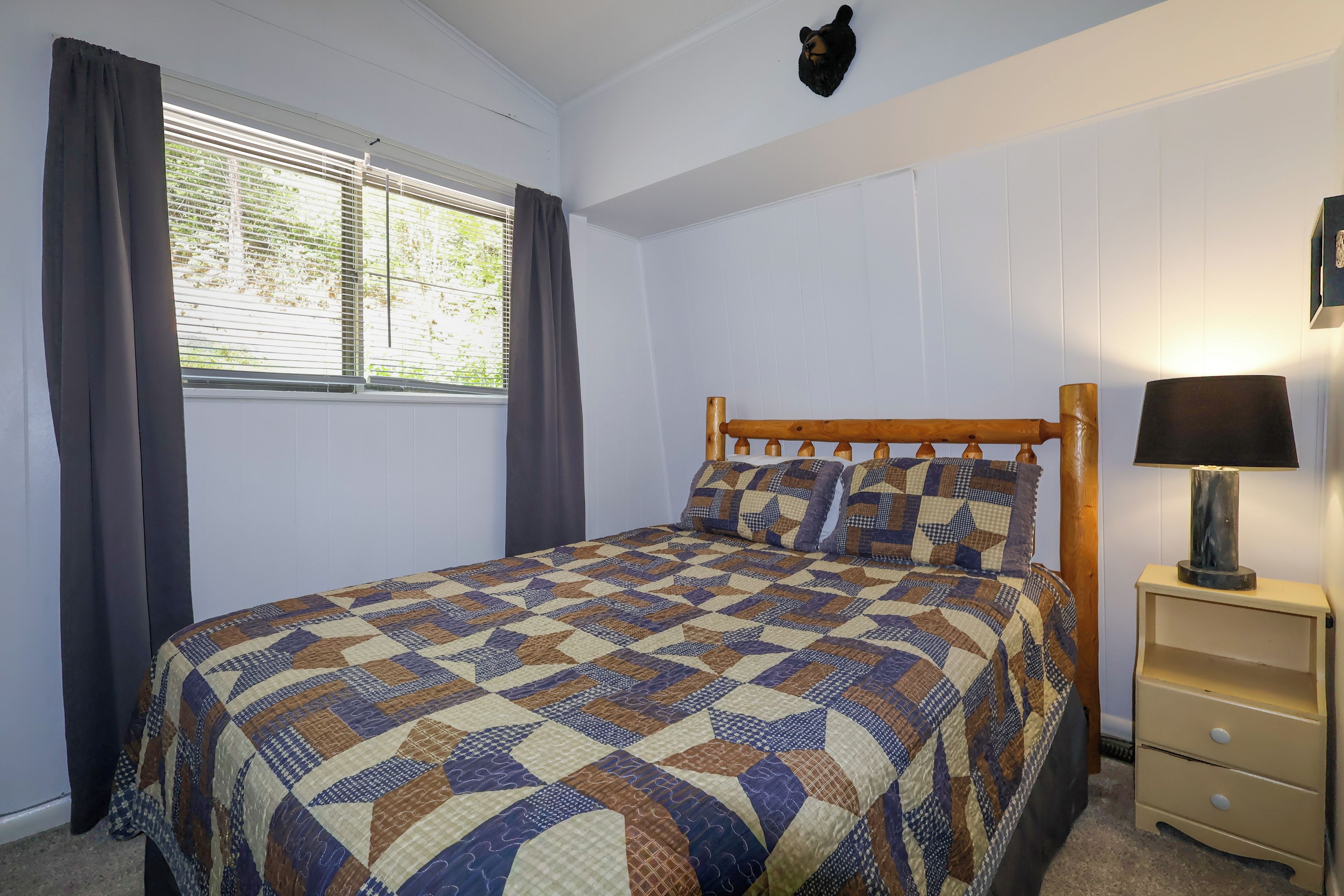 Un dormitorio con cama de madera, una mesita de noche con lámpara y una ventana con cortinas.