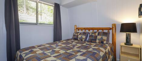 Un dormitorio con cama de madera, una mesita de noche con lámpara y una ventana con cortinas.