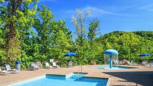 Un espace piscine doté de chaises longues et de parasols, entouré d’arbres et surplombé d’un ciel dégagé.