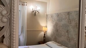 Un dormitorio con un espejo grande, una cama con toallas dobladas cuidadosamente, una lámpara de pared y una pared con textura.