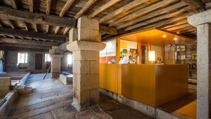 A stone-floored room with a wooden ceiling and a reception desk. - Torre Lombarda (Allariz)