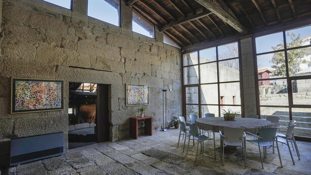 A rustic stone interior with a stone fireplace, large windows, and a round table with chairs. - Torre Lombarda (Allariz)