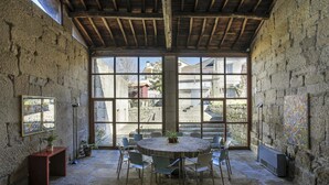 A stone-walled room with a round table and chairs, large windows, and a wooden ceiling. - Torre Lombarda (Allariz)