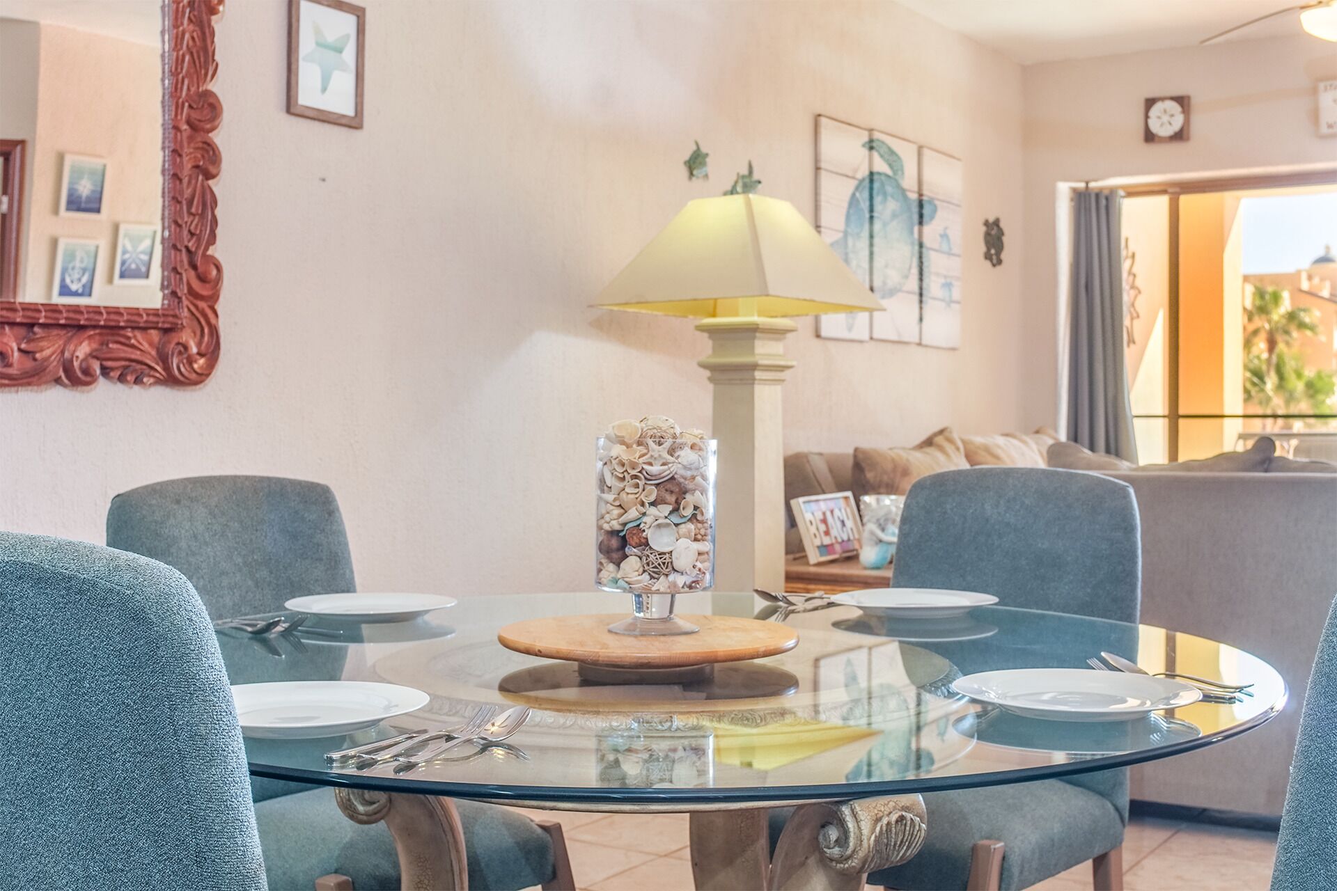 Un coin repas avec une table en verre, des chaises et une lampe. Un tableau encadré est accroché au mur, et un canapé se trouve à l’arrière-plan.