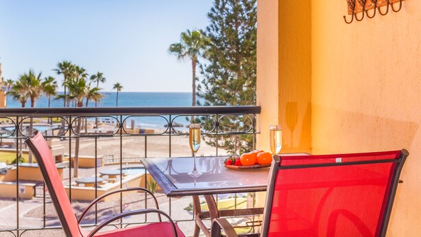 A balcony with a table, chairs, a bottle of champagne, and a plate of fruit. - Princesa Resort B-201 Slow M'Ocean Cottage Ocean View Private Condo (Puerto Penasco)