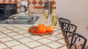 A kitchen with a tiled backsplash, a stainless steel sink, a coffee maker, a wine rack, and a fruit bowl with oranges and strawberries. - Princesa Resort B-201 Slow M'Ocean Cottage Ocean View Private Condo (Puerto Penasco)