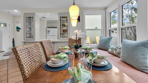 A dining area with a wooden table set for four, surrounded by wicker chairs, a blue cushioned bench, and a hanging light fixture. - **SEA CAPTAIN'S HAVEN** Luxury Villa & Pool + Last Key White Glove Service... (Key West)