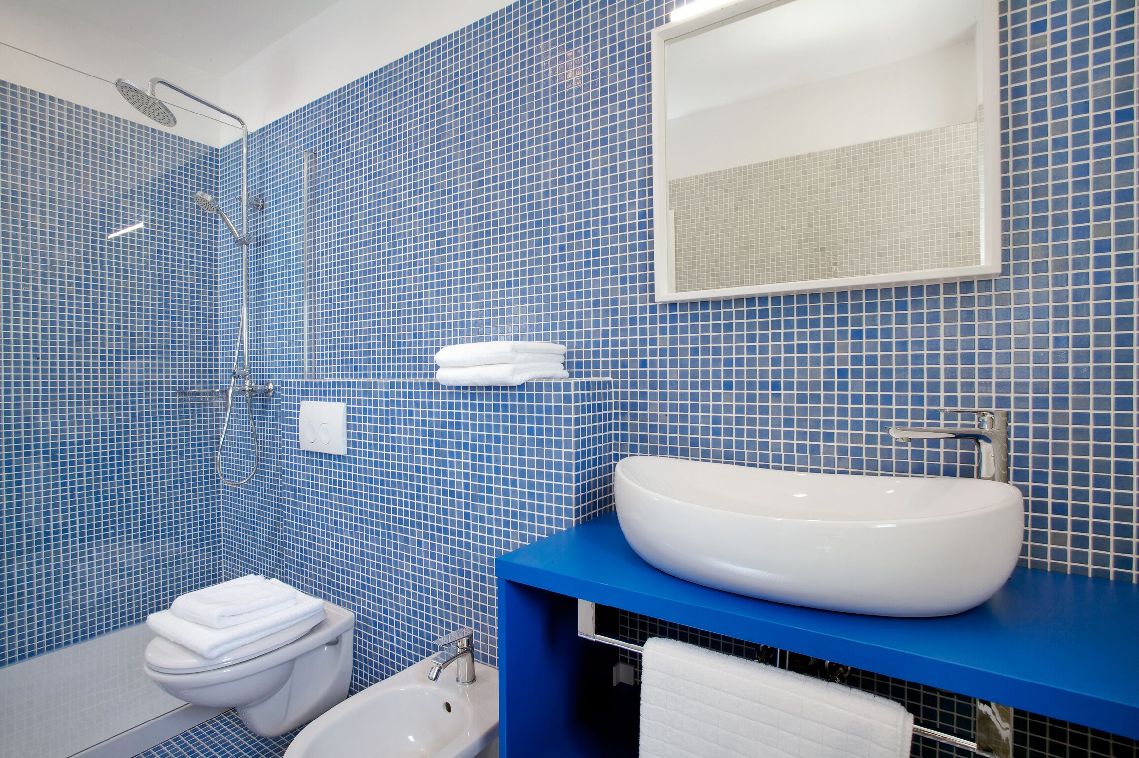 Un baño con mosaicos azules, un lavabo blanco, un inodoro y una ducha.
