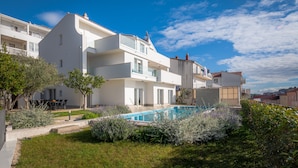 Un moderno edificio residencial con piscina, rodeado de jardines bien cuidados y un cielo azul despejado.