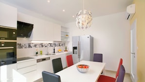 Una cocina moderna con armarios blancos, un horno Bosch, un refrigerador y una mesa de comedor con sillas.