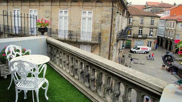 Ein Innenhof mit Steinbalustrade, einem weißen Metalltisch und -stühlen sowie einem Gebäude mit rotem Ziegeldach.