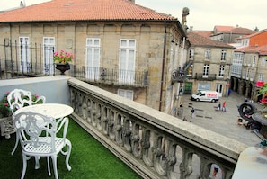 Ein Innenhof mit Steinbalustrade, einem weißen Metalltisch und -stühlen sowie einem Gebäude mit rotem Ziegeldach.