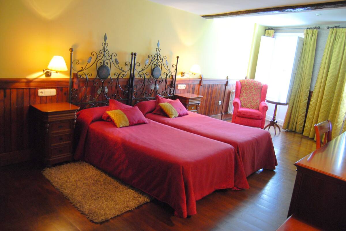 A room with two beds, wooden furniture, a small table, and a chair.