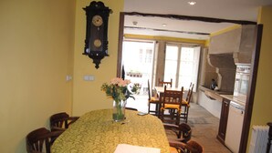 Ein Essbereich mit einem Tisch, der mit einer gemusterten Tischdecke bedeckt ist, umgeben von Holzsesseln. Auf dem Tisch steht eine Vase mit Blumen.