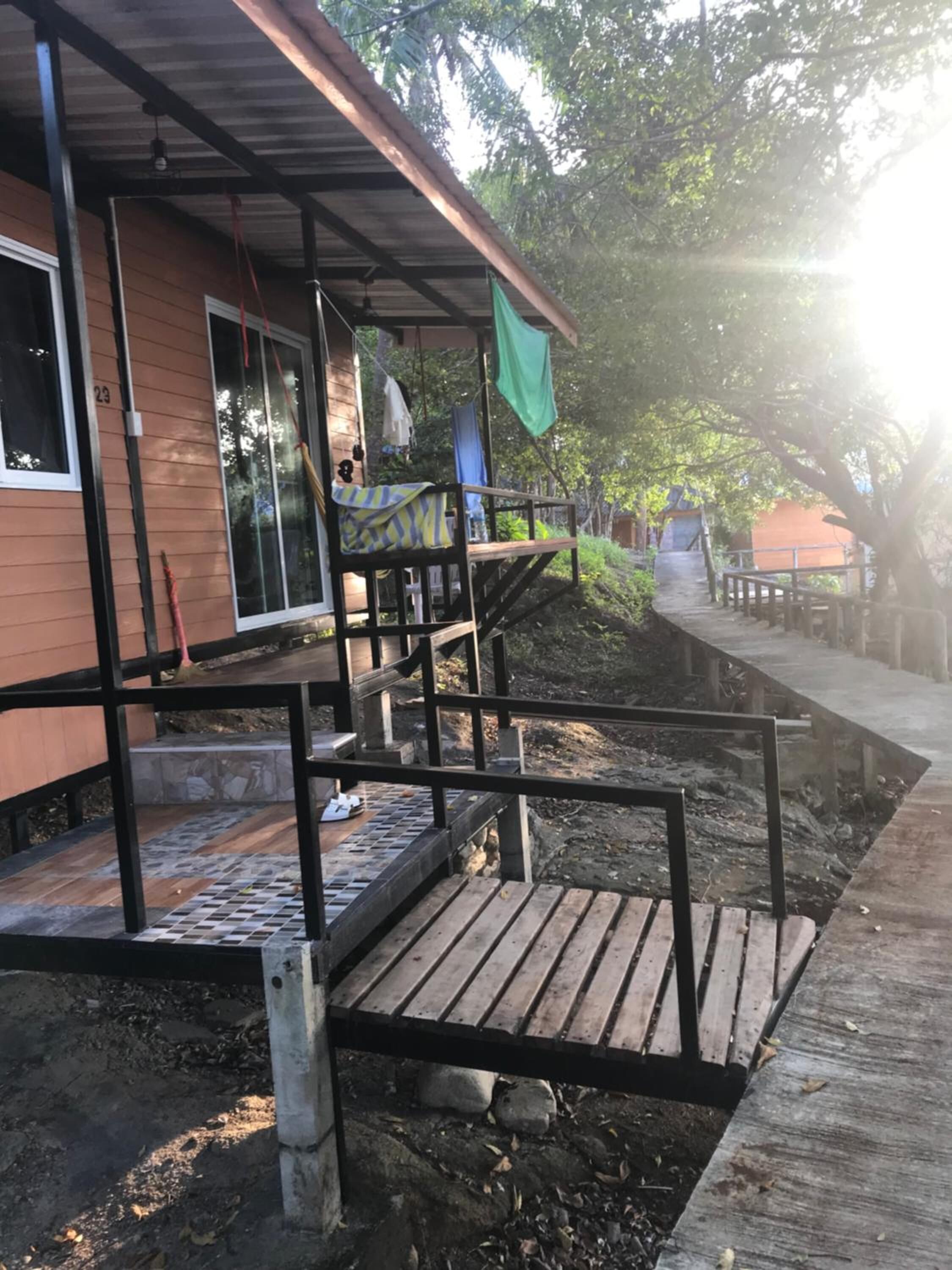 Una casa de madera con un porche, una escalera y un pequeño espacio exterior con un banco.