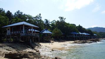Una propiedad frente a la playa con varias casas sobre pilotes, una playa de arena y un litoral rocoso.